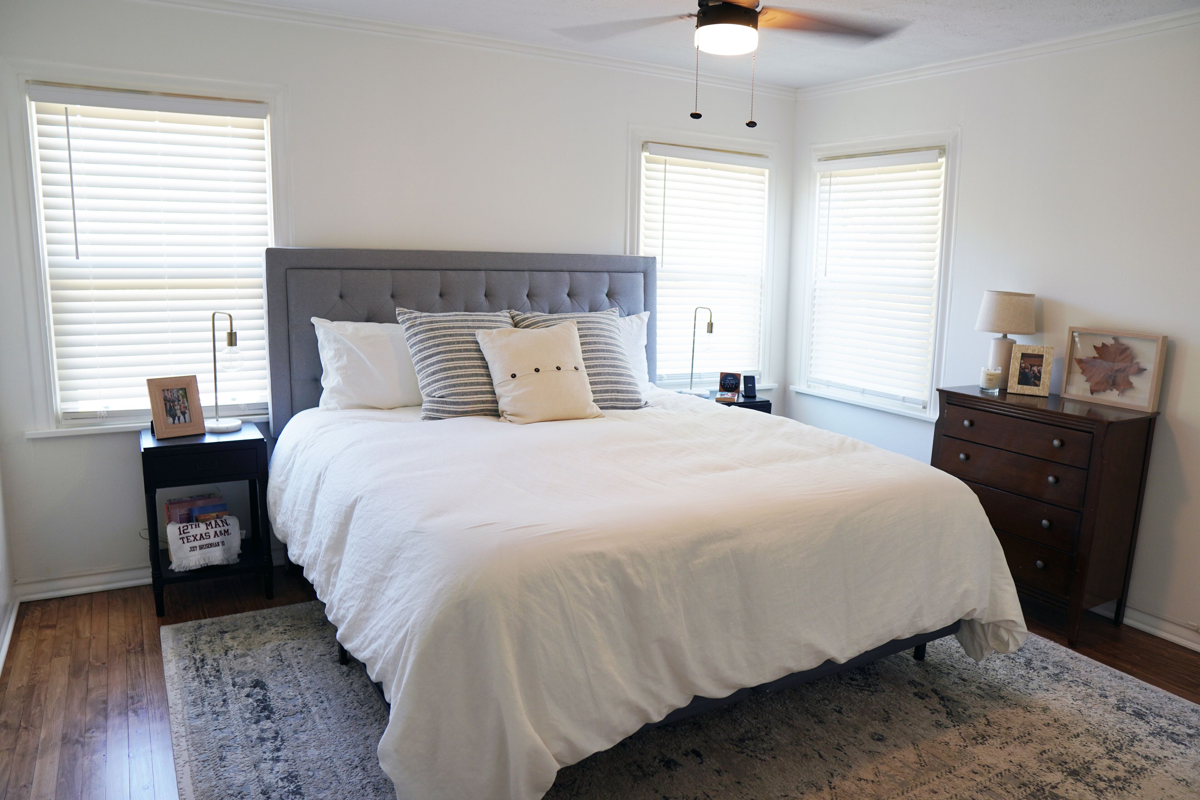 A bedroom with a large bed, two nightstands, a dresser, and a ceiling fan.