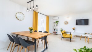 A modern living room with a wooden dining table, black chairs, a yellow armchair, a bookshelf, and a TV mounted on the wall. - Lovely home in Valbandon (Valbandon)