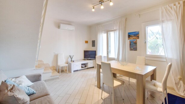 A modern, well-lit living room with a sofa, a dining table, and a TV. - Lovely home in Valledoria with WiFi (Valledoria)