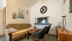 Ein gemütliches Wohnzimmer mit einer Couch, einem Holztisch, einem grauen Sessel und einem an der Wand befestigten Fernseher.
