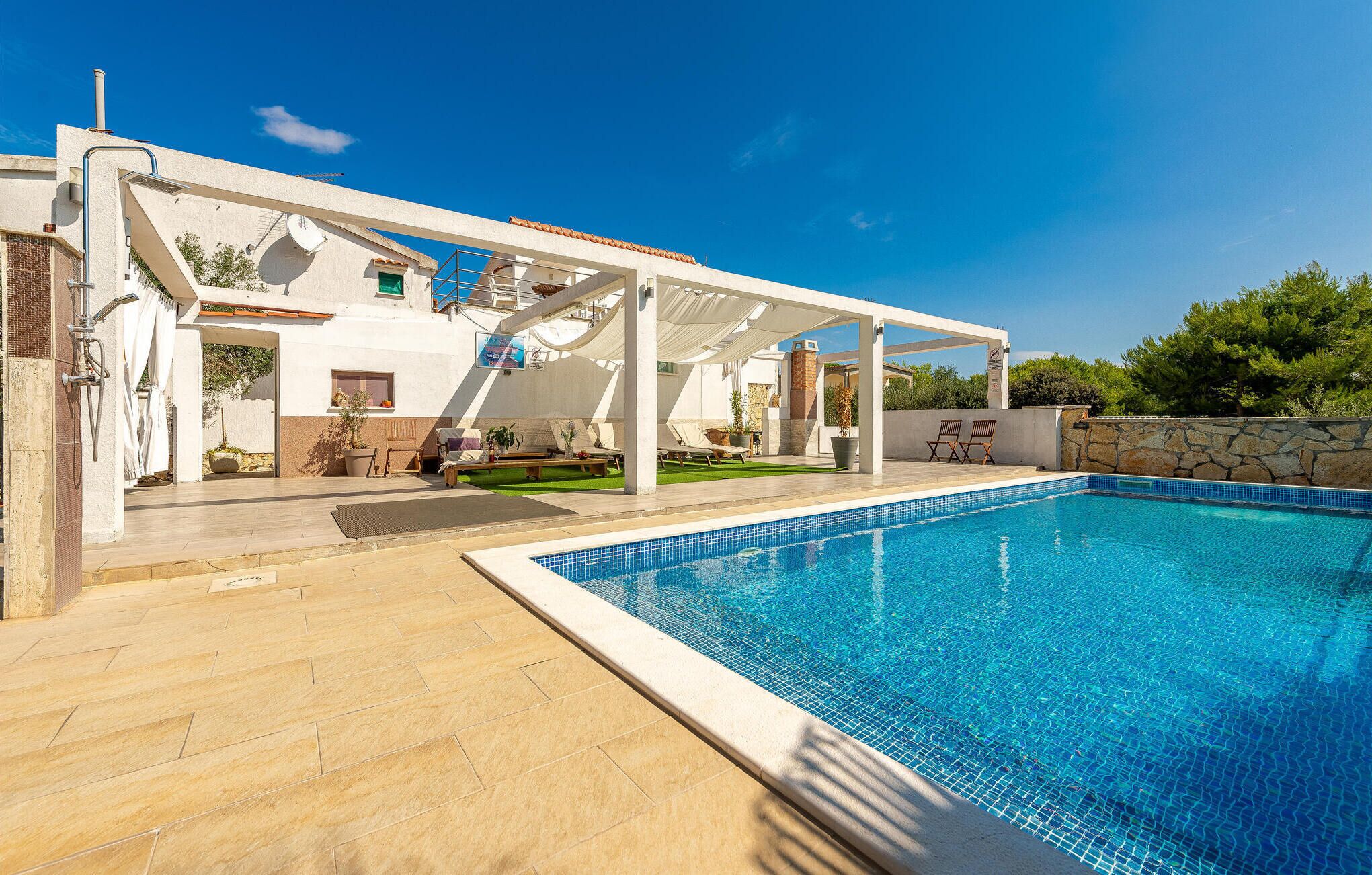 A poolside area with a covered seating area, a stone wall, and a clear blue pool.