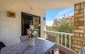 A balcony with a table set for dining, a glass vase with flowers, and a view of pink flowers and greenery. - Gorgeous apartment in Vir with WiFi (Vir)