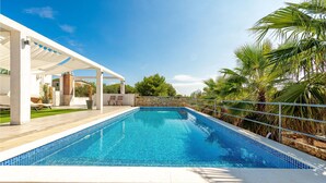 Ein Pool mit einer weißen Pergola, einer Steinmauer und Palmen.