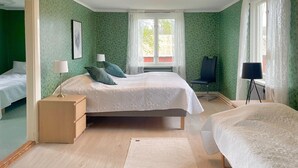 Ein Zimmer mit zwei Betten, einem Fenster mit Vorhängen, einem Schreibtisch mit Lampe und einem Stuhl.