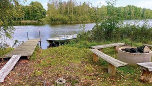 Eine Holzsteganlage am Seeufer mit einem Boot, Picknicktischen und einer Feuerstelle.