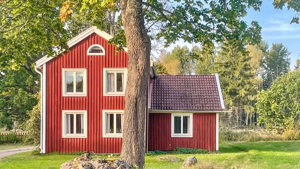 Ein rotes Holzhaus mit geneigtem Dach und einem daran angebauten Anbau.