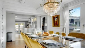 Un coin repas avec une longue table dressée pour six personnes, entourée de chaises jaunes, d’un lustre et d’une grande fenêtre offrant une vue dégagée.