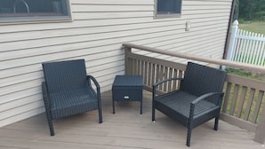 Eine überdachte Terrasse mit zwei Korbstühlen und einem kleinen Tisch.