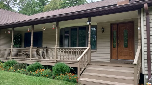 Ein zweigeschossiges Haus mit überdachter Veranda, Eingangstür und einem kleinen Vorgarten mit Blumen.