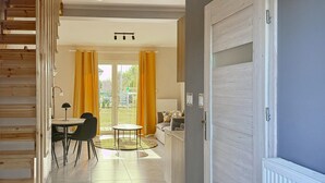 A modern interior with a dining area, a sofa, and a view through a glass door to an outdoor space. - 2 bedroom nice home in Grzybowo (Grzybowo)