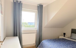 A bedroom with a window, a radiator, a bed with a patterned bedspread, a bedside table with a lamp, and a headboard. - 2 bedroom nice home in Grzybowo (Grzybowo)