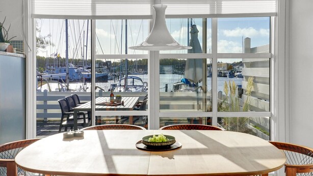A dining area with a large window overlooking a marina, featuring a table with a bowl of fruit and a bottle. - Amazing home in Ebeltoft with sauna (Ebeltoft)