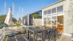 A modern outdoor dining area with a large table and chairs, a potted plant, and a view of the sea with sailboats in the background. - Amazing home in Ebeltoft with sauna (Ebeltoft)
