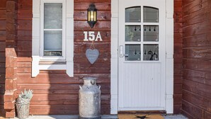 Une cabane en bois avec une porte blanche, une fenêtre dotée d’un volet et une lanterne au-dessus de la porte.