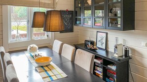 Un coin repas avec une table dressée pour deux personnes, un buffet noir aux portes vitrées et une fenêtre donnant sur l’extérieur.