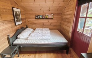 Ett sovrum i en stuga, inrett med träpanel, som innehåller en säng, ett litet bord och en hylla med böcker.