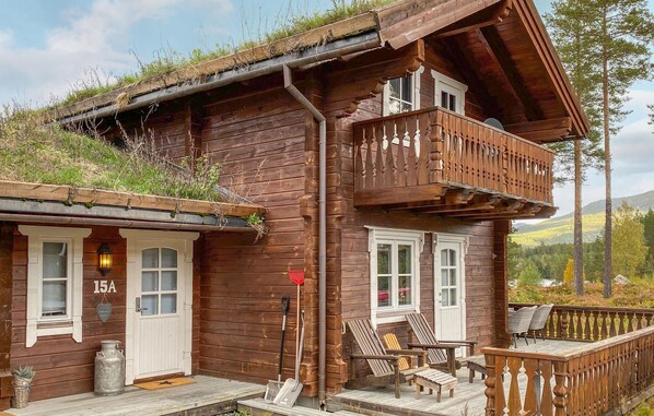 En stuga byggd av trä med en balkong, en veranda med sittplatser och en synlig brevlåda.
