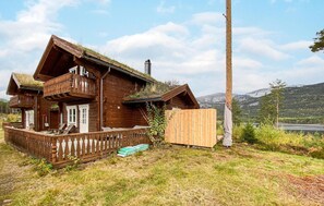 Ett trähus med en balkong, ett trästaket och utsikt över berg i bakgrunden.