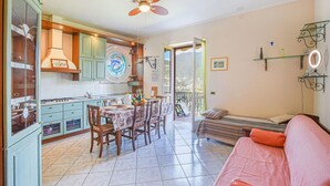 Un vaste espace de vie comprenant une table à manger, des chaises et un canapé. On peut apercevoir une cuisine avec des meubles de couleur turquoise et une cuisinière.
