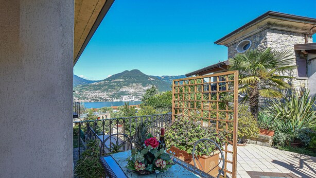 A balcony with a view of a coastal town, a wooden trellis, and potted plants.