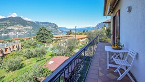 A balcony with a table and chairs overlooking a scenic view of a lake, mountains, and buildings.