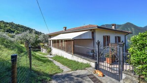 Une maison avec un porche abrité, une cour clôturée et une montagne en arrière-plan.