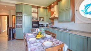Une cuisine avec des meubles de couleur turquoise, une table à manger dressée avec des assiettes et des couverts, et une fenêtre donnant sur le ciel.
