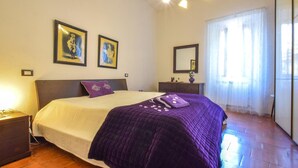 Une chambre à coucher comprenant un lit, des tables de chevet, une commode, un miroir et deux œuvres d’art encadrées accrochées au mur.