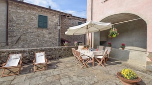 Une terrasse extérieure avec une table et des chaises, un pot de fleurs suspendu et un mur en pierre.