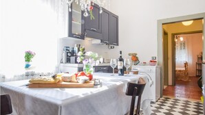 Une cuisine avec une table à manger dressée pour deux personnes, une machine à café et une bouteille de vin.