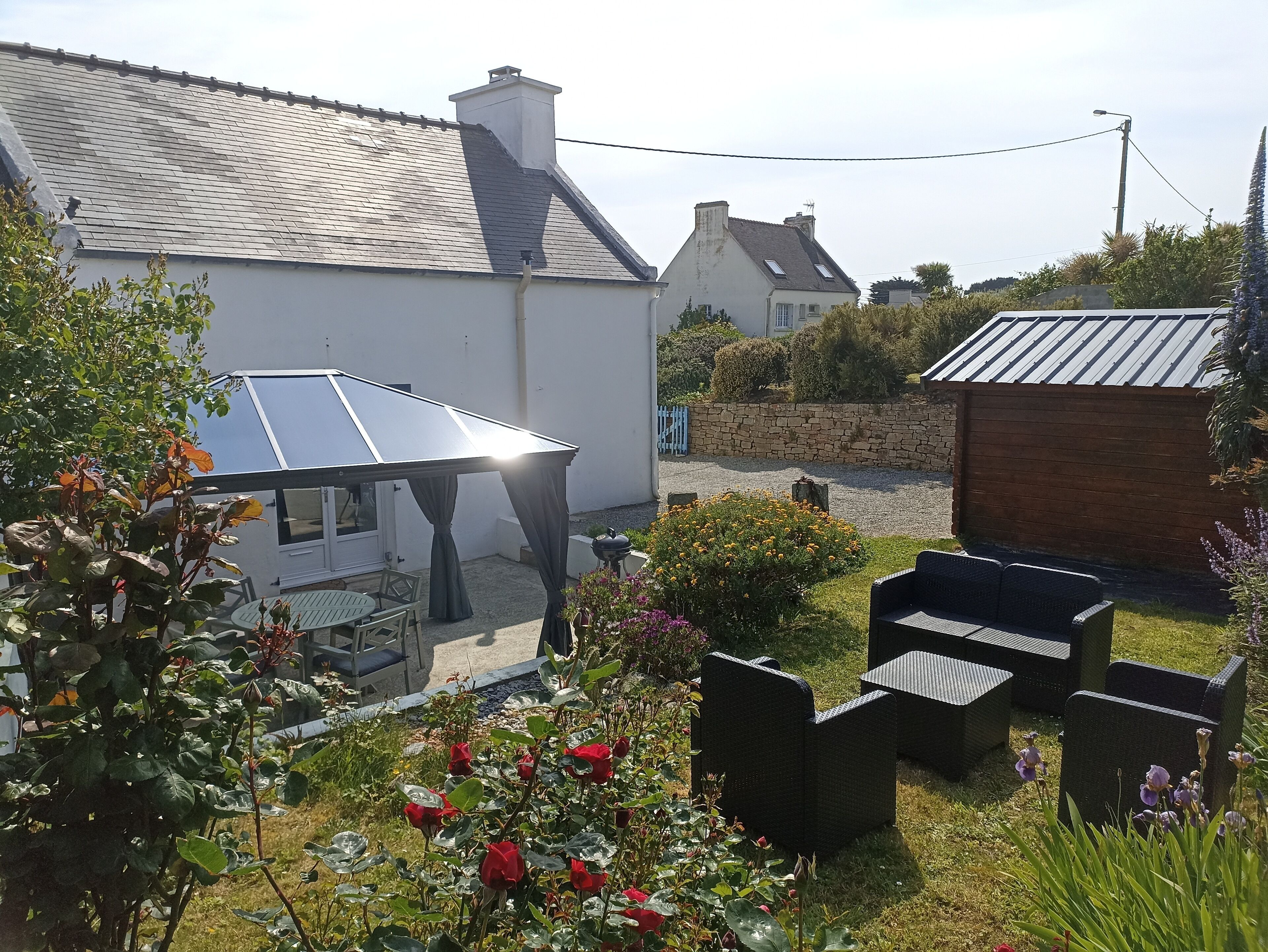 A house with a sloped roof, a garden with flowers and plants, outdoor furniture, and a solar panel.
