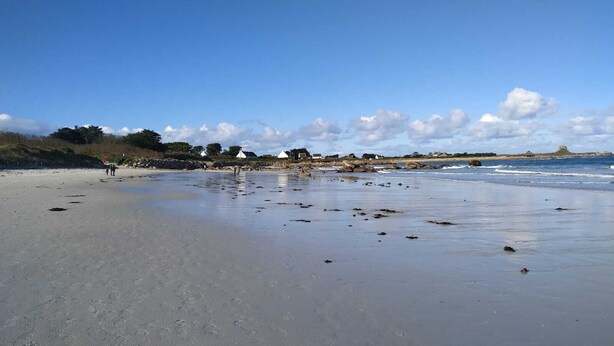 A beach with footprints, a few people, and white structures in the distance. - House by the sea (Plouguerneau)