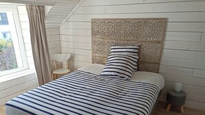 A bedroom with a striped bedspread, a decorative headboard, a bedside table, and a lamp. - House by the sea (Plouguerneau)