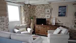 A living room with stone walls, a wooden cabinet, a television, and two white sofas. - House by the sea (Plouguerneau)