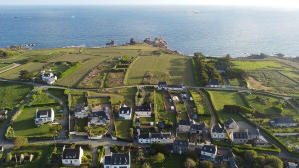 An aerial view of a coastal village with houses, green fields, and rocky outcrops. - House by the Sea (Plouguerneau)