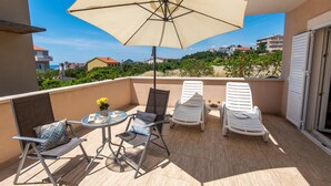 Un balcon avec une table, des chaises et un parasol. On aperçoit des bâtiments au loin.
