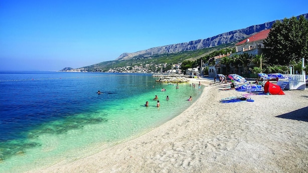 Une plage avec une eau cristalline, des gens qui se baignent et des parasols sur le sable.