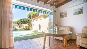A living room with a glass table, beige sofa, and a view of a backyard with a pool and greenery.