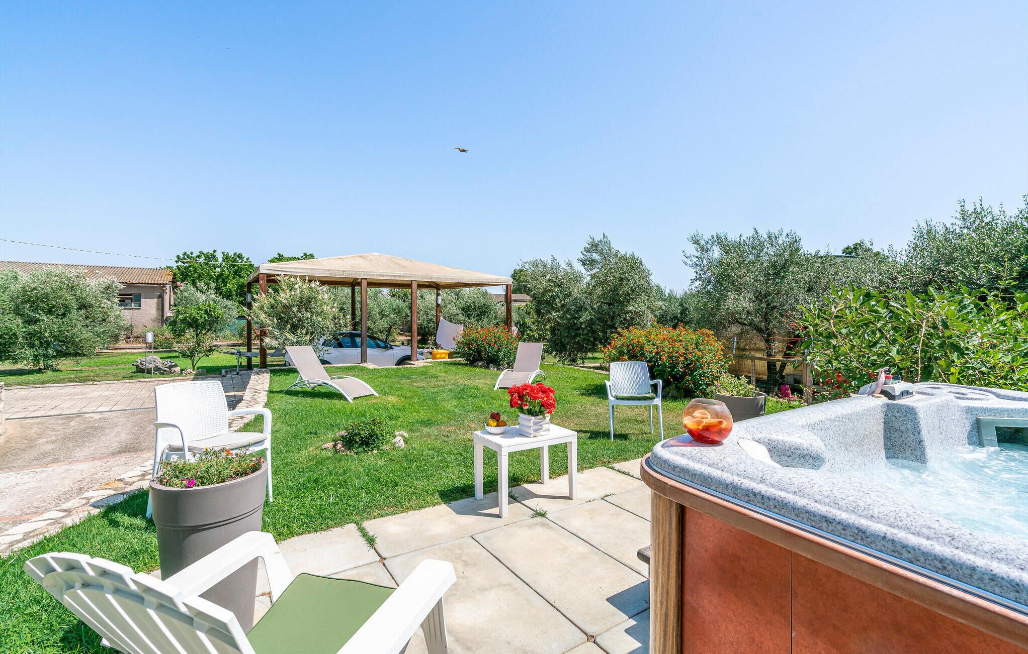 A backyard with a hot tub, lounge chairs, a pergola, and a garden.