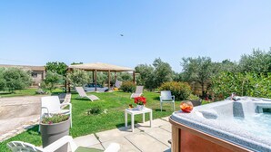 Een achtertuin met een jacuzzi, lounge stoelen, een pergola en een tuin.
