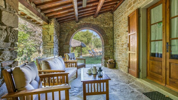 A stone-walled patio with a wooden bench and table, a thatched umbrella, and a view of the garden. - Cozy home in Castiglion Fiorentino (Castiglion Fiorentino)