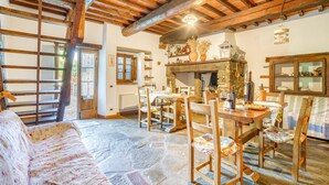 A rustic dining area with a stone fireplace, wooden furniture, and a view of the outdoors. - Cozy home in Castiglion Fiorentino (Castiglion Fiorentino)