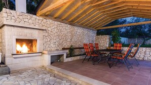 Une terrasse extérieure avec une cheminée en pierre, une table à manger avec des chaises et un mur en pierre.