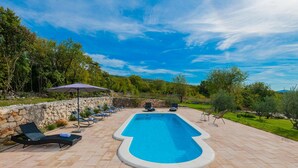 A rectangular swimming pool with a stone wall and lounge chairs on one side, surrounded by greenery and a clear sky. - Awesome home in Vinjani Donji (Vinjani Donji)