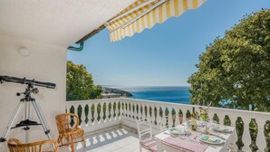 Un balcone con un telescopio, sedie in vimini e un tavolo apparecchiato per mangiare, vista sul mare.