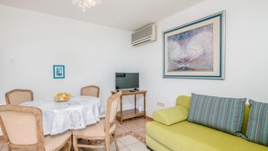 Un soggiorno con zona pranzo, un divano verde, una TV su un mobile in legno e un quadro appeso al muro.
