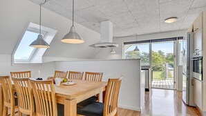 A modern kitchen with a dining area, featuring wooden furniture, pendant lights, and a view to the outdoors.