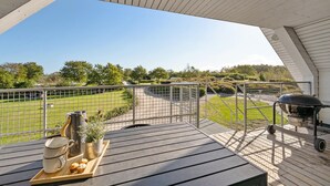 A balcony with a view of a green field and a barbecue grill.