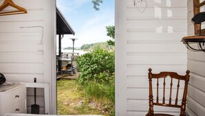 A room with a wooden chair, a hanging heart-shaped decoration, and a view of a patio with outdoor furniture and greenery. - Amazing home in Ronneby with house sea view (Ronneby)