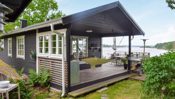 A cabin with a deck overlooking a lake, featuring a hammock, outdoor seating, and a view of the water. - Amazing home in Ronneby with house sea view (Ronneby)